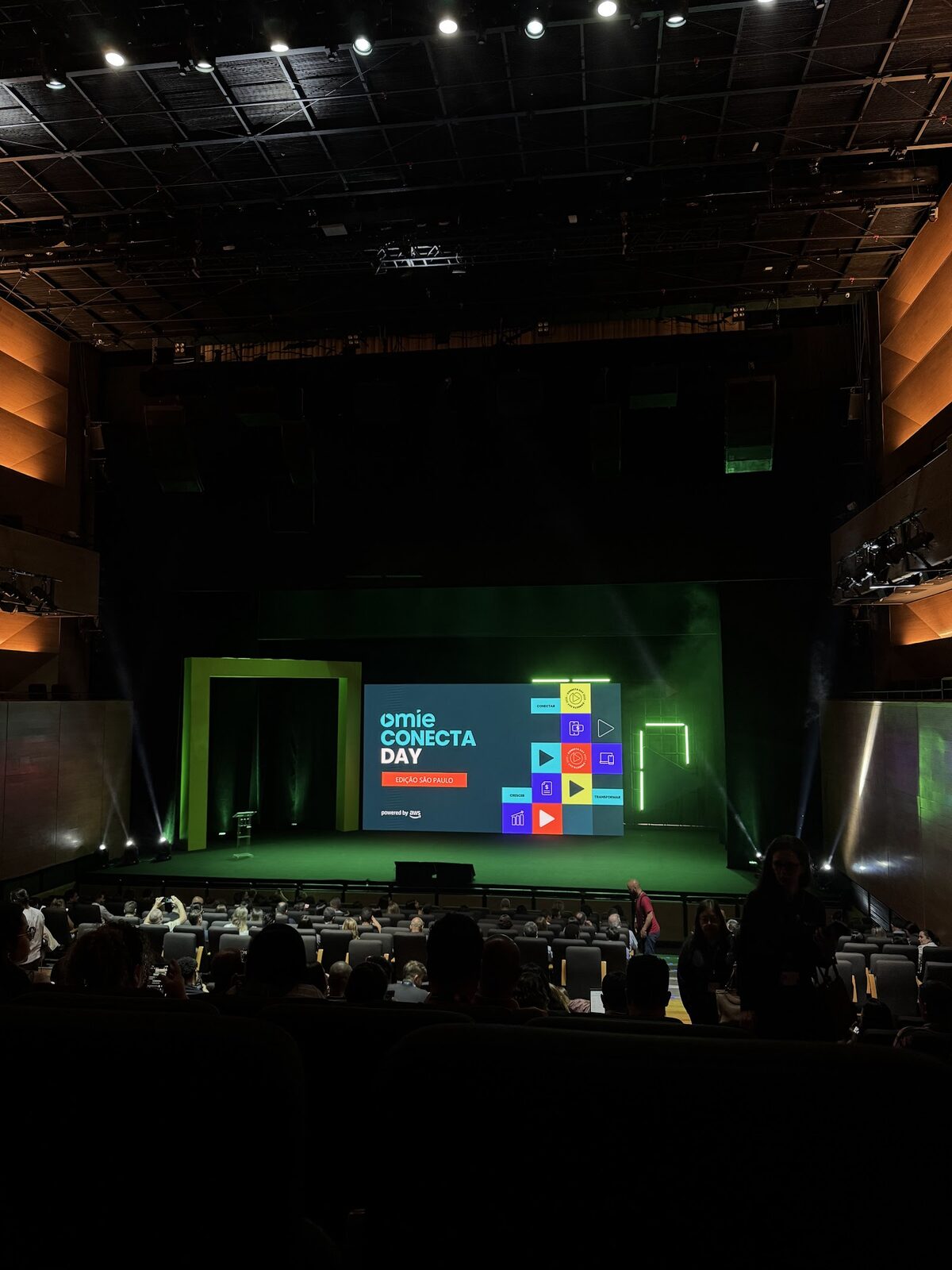 Palco de auditório com cenografia de portal amarelo e moldura verde neon em sala de pé-direito alto