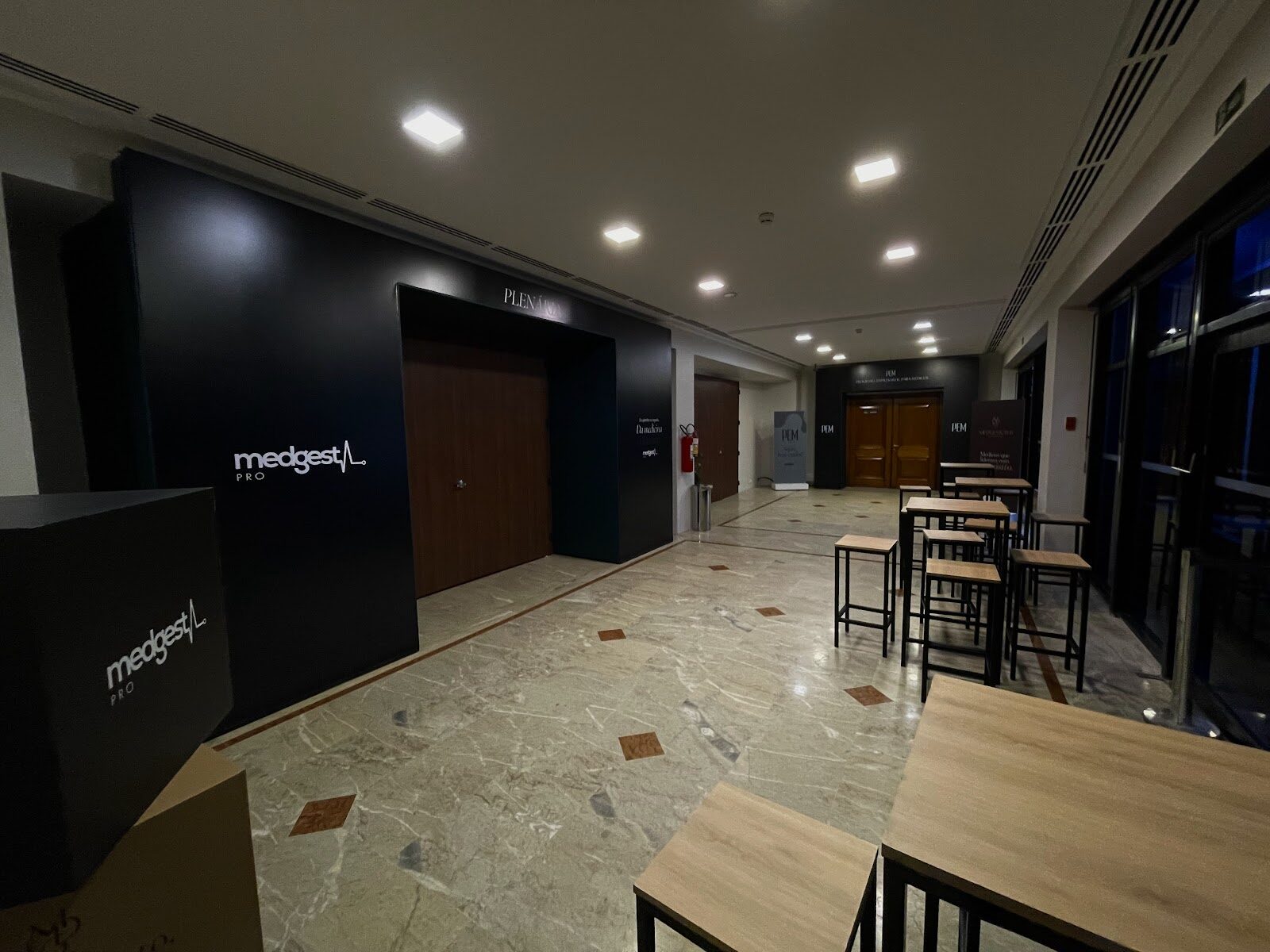Parede cenográfica preta de acesso à plenária em corredor com piso de mármore de evento corporativo