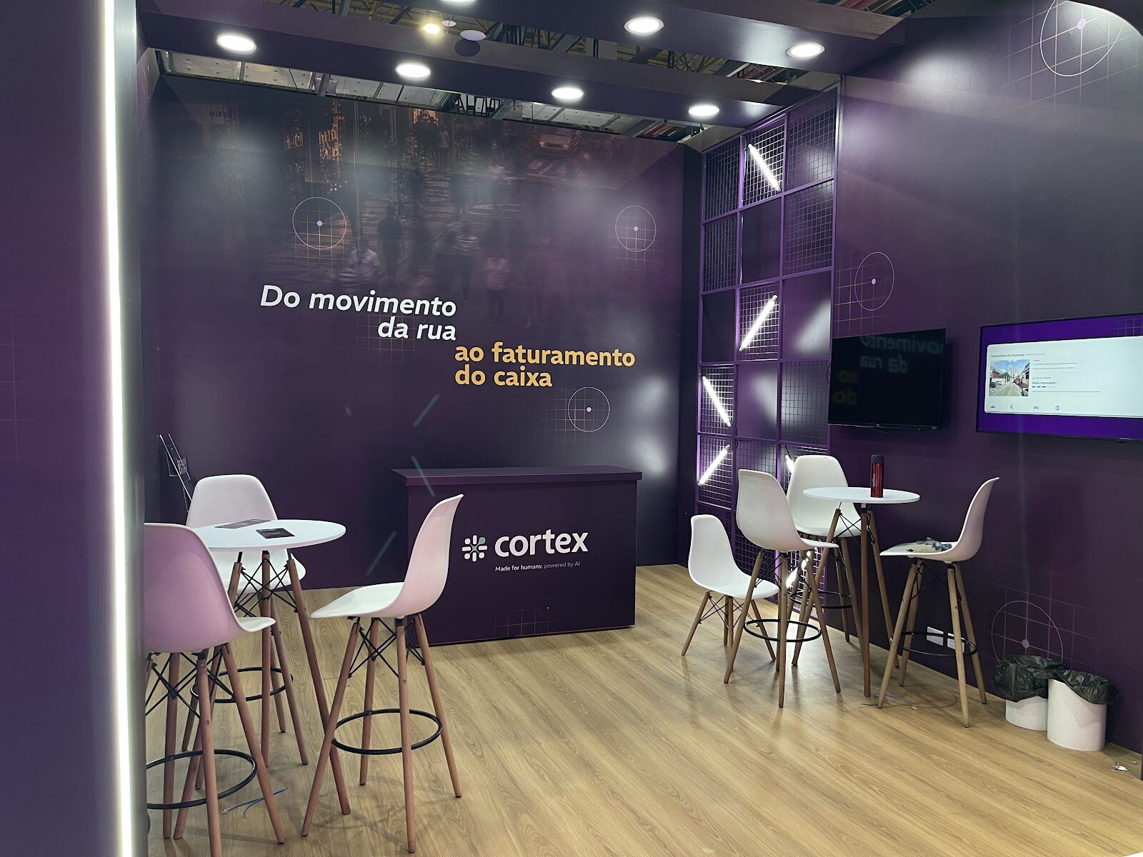 Interior de stand fechado com mobiliário, telas e iluminação roxa