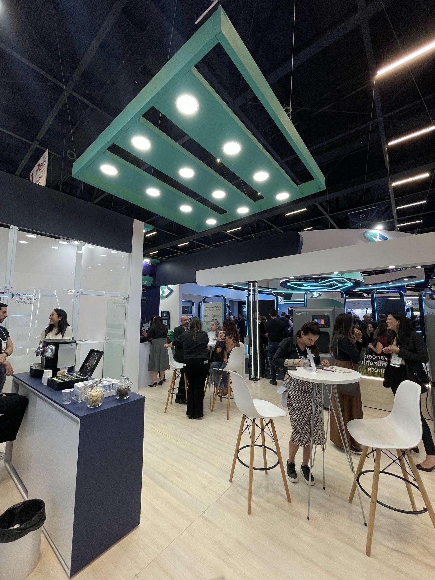 Lounge com mesas altas e estrutura suspensa iluminada em stand de feira