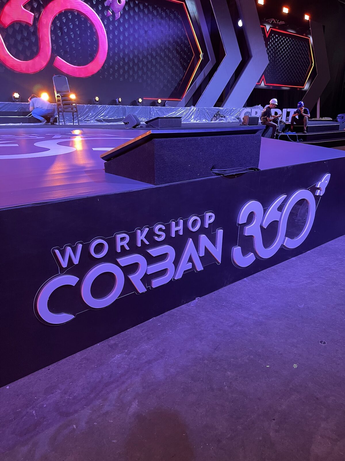 Bastidores de montagem com técnico ajustando refletores em palco cenográfico de evento
