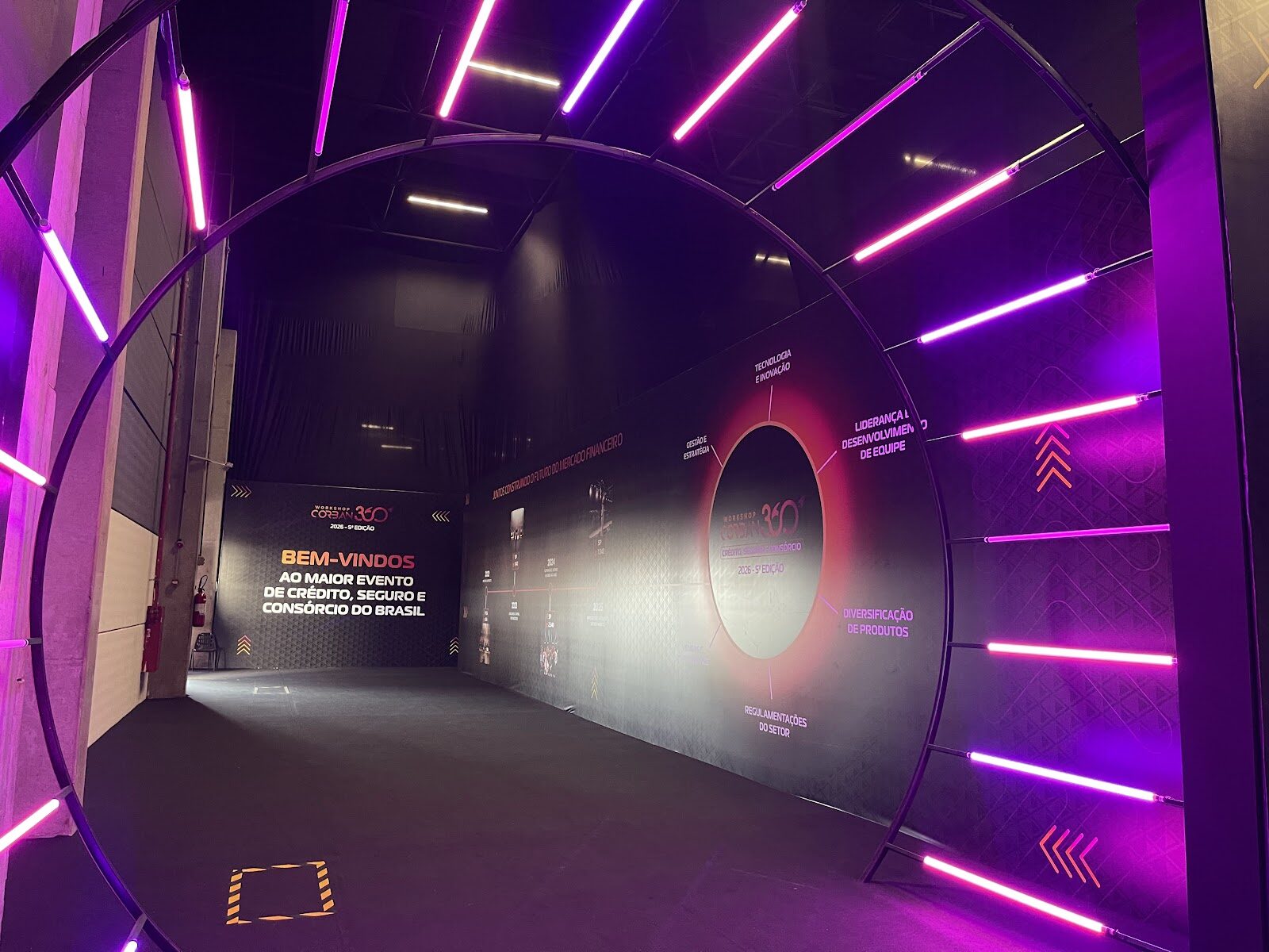 Túnel cenográfico com arcos de neon rosa e roxo em evento corporativo CORBAN