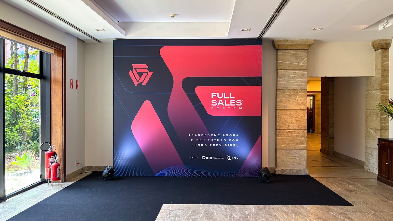 Backdrop cenográfico vermelho e preto de evento corporativo montado em lobby com piso de mármore