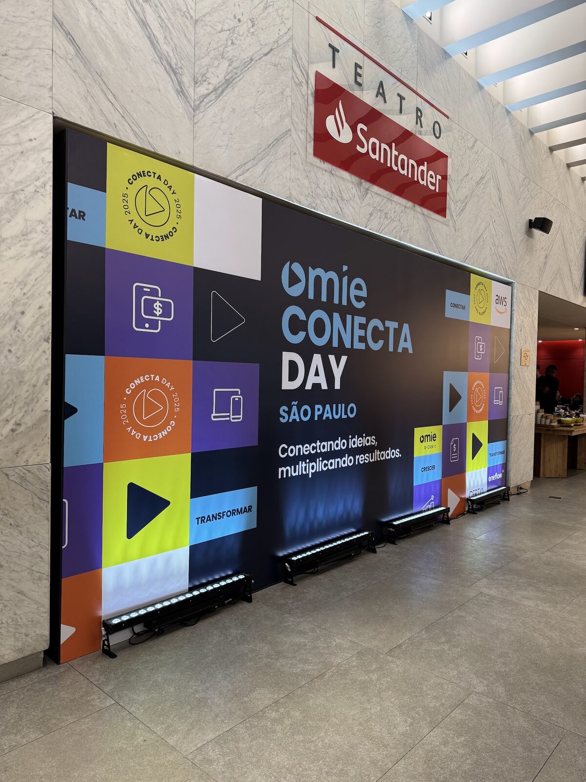 Painel cenográfico de entrada com testeira gráfica colorida e barras de luz no piso em evento corporativo