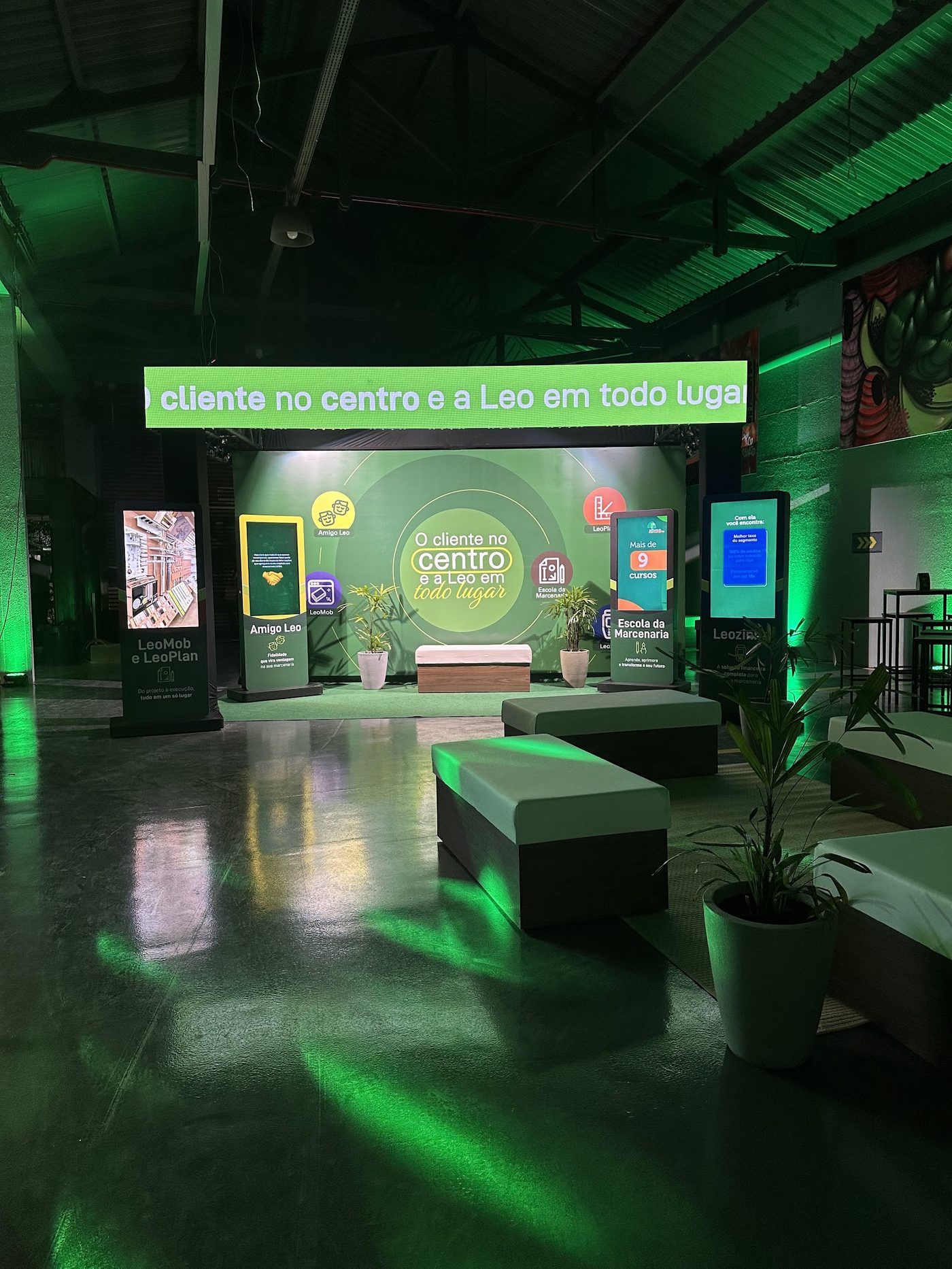 Stand corporativo com painéis digitais, totens interativos e iluminação cenográfica verde em feira