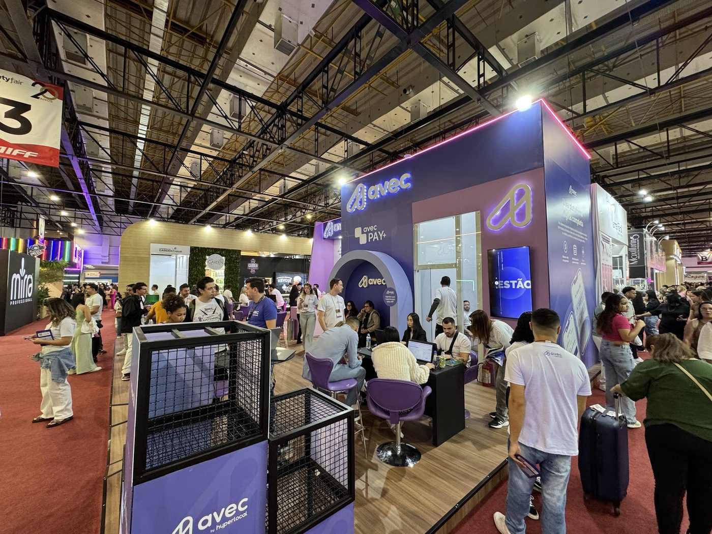 Stand construído com testeira iluminada em pavilhão de feira de cosméticos, corredor movimentado ao redor