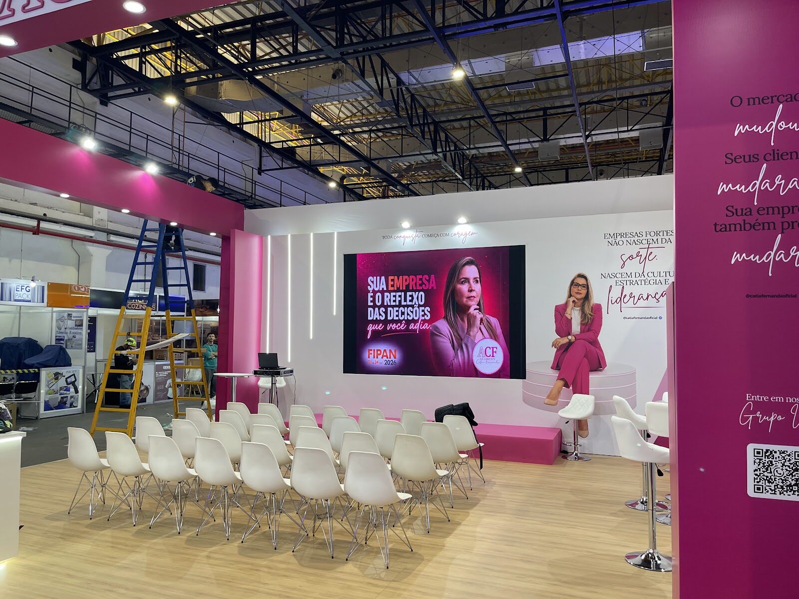 Stand em fase final de montagem na Fipan, com escada, cadeiras de auditório e telão, pavilhão ainda em obra