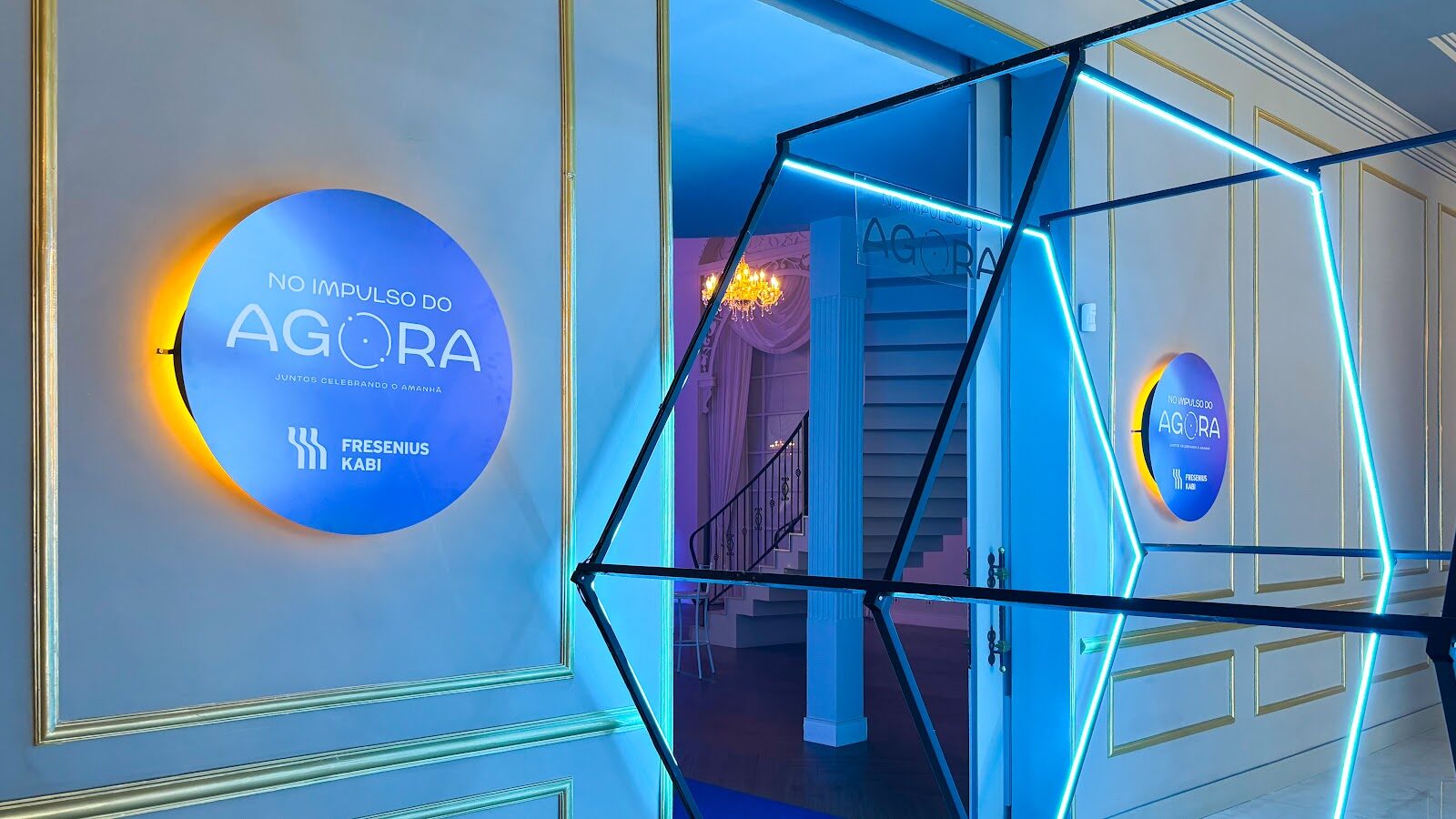 Entrada de salão com estruturas neon hexagonais suspensas e iluminação cenográfica