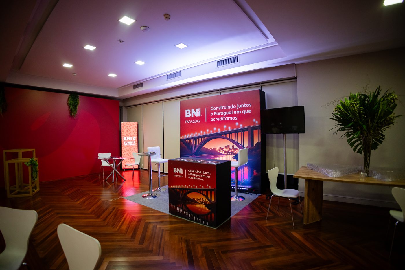 Módulo de atendimento da BNI Paraguay na área de parceiros do BNI Summit 26 SP, com backdrop iluminado, balcão e TV