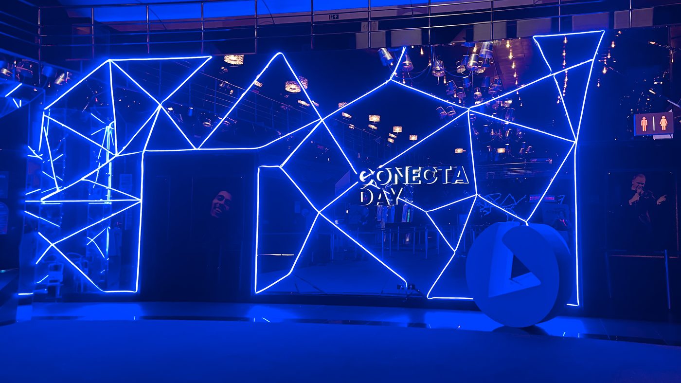 Pórtico cenográfico em neon flex com formas geométricas e símbolo Omie no Conecta Day, Espaço Unimed