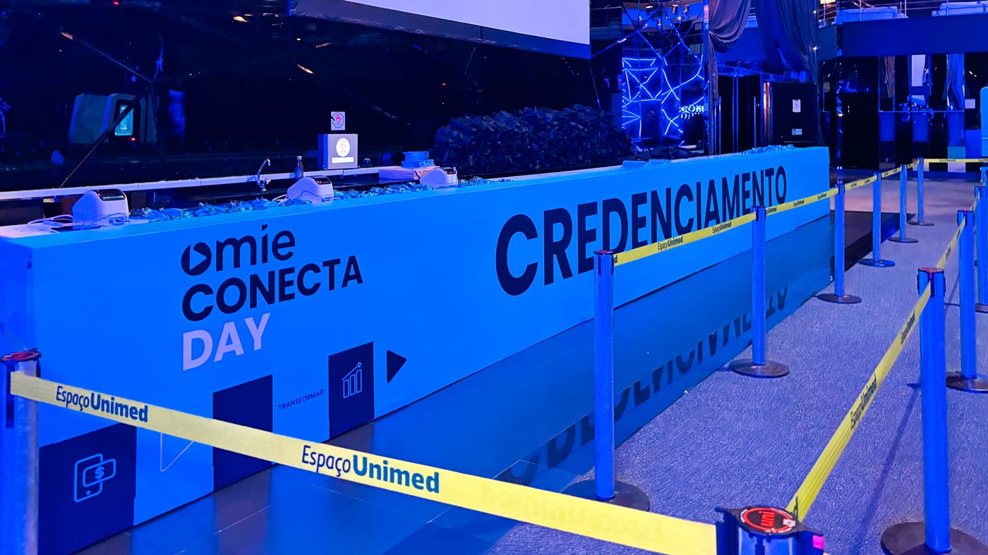 Balcão de credenciamento de 11,43 metros revestido em placa PS adesivada com a marca Omie