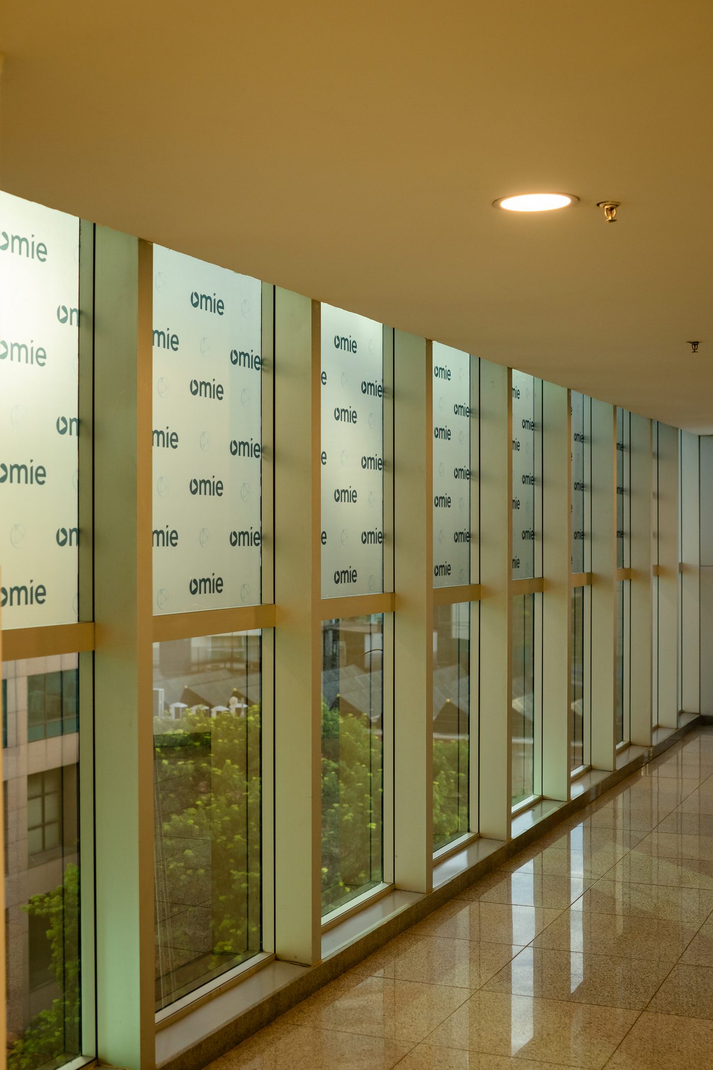 Corredor envidraçado do foyer com adesivo modulado do logotipo Omie aplicado nos panos de vidro