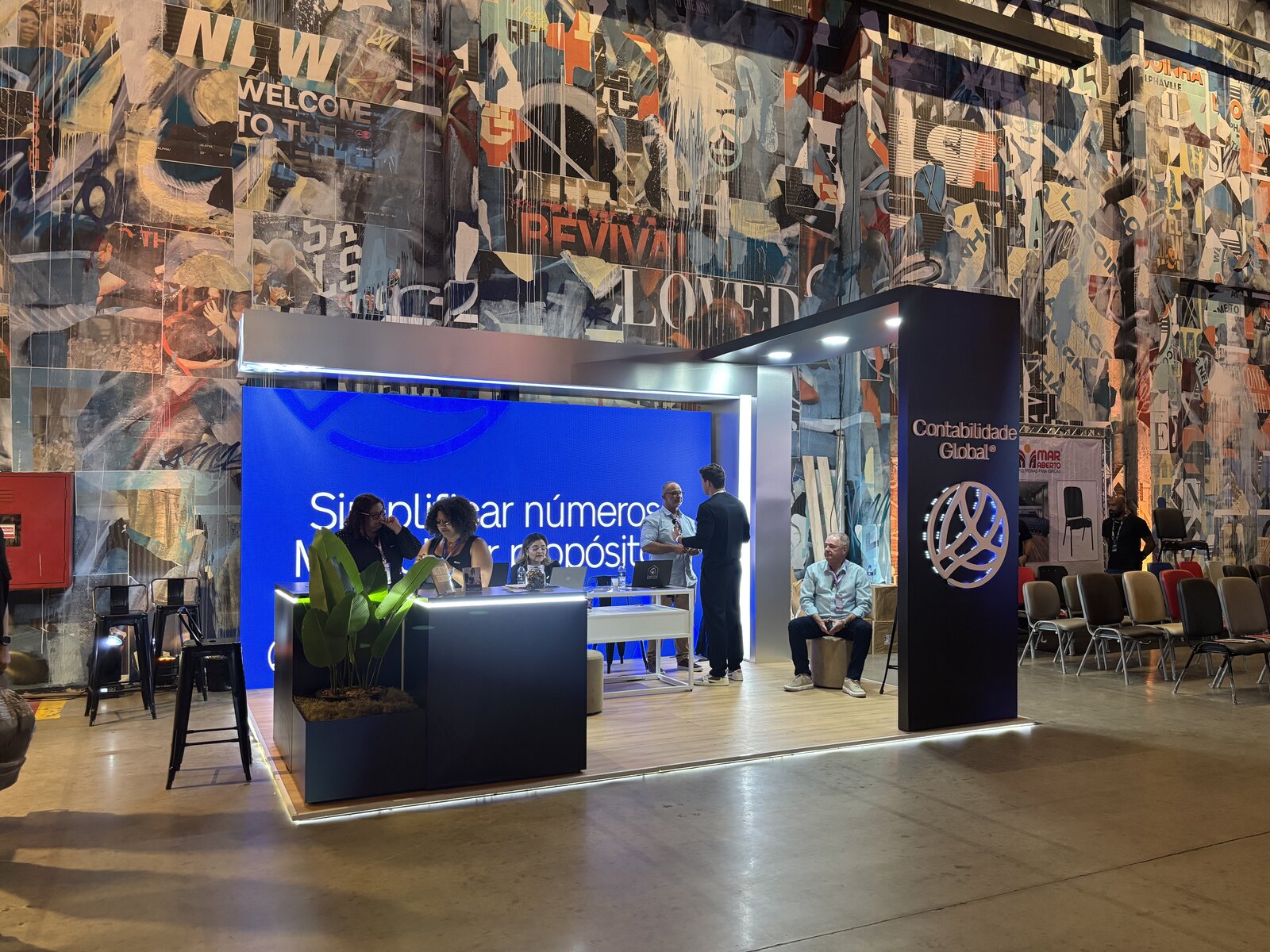 Vista geral do stand da Contabilidade Global com torre retroiluminada, painel de LED e balcão com jardineira integrada, montado pela Atom Cenografia