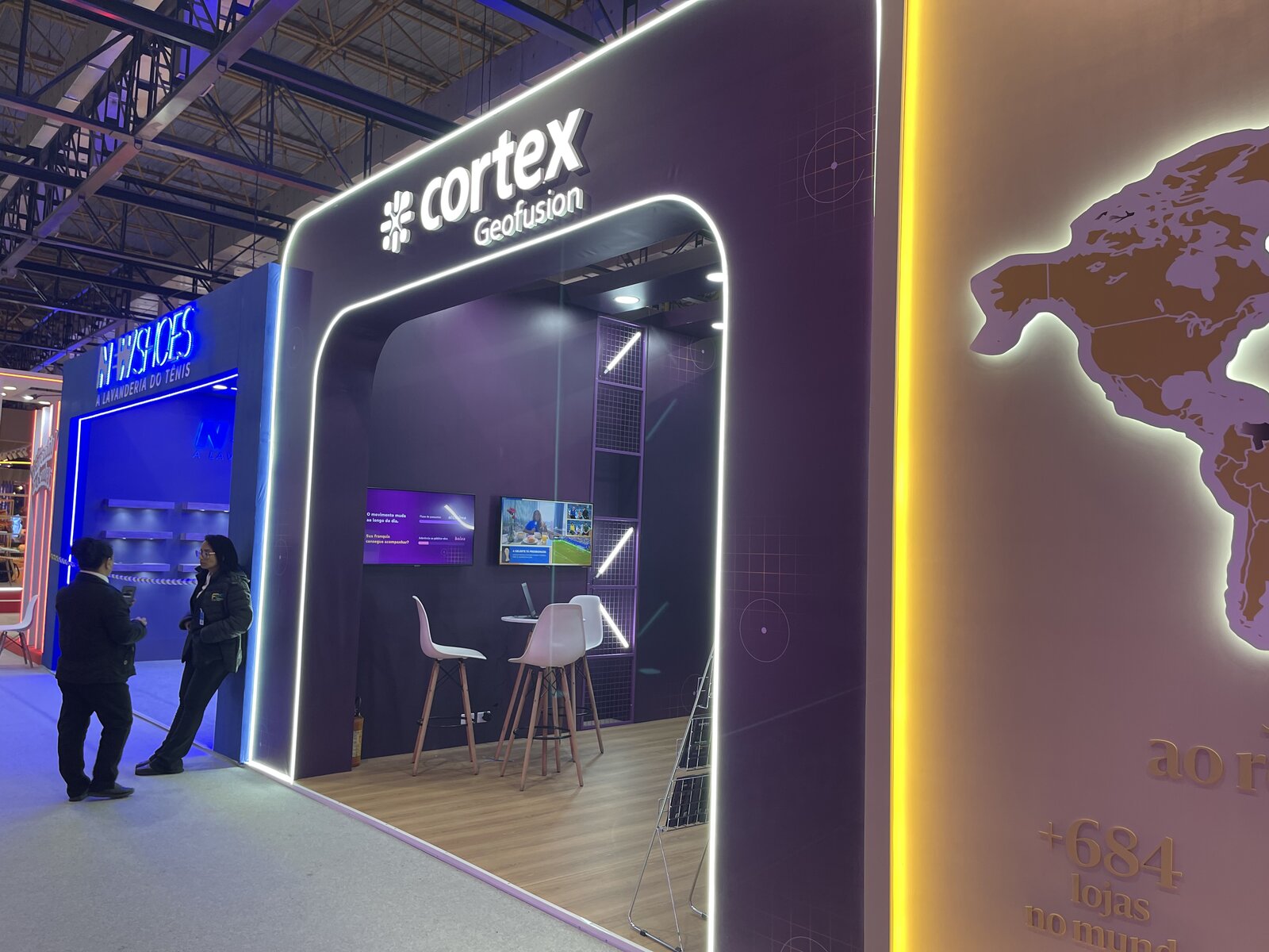 Interior do stand da Cortex Geofusion com painéis gradeados, TVs para demonstração de produto e mesa bistrô, montado pela Atom Cenografia